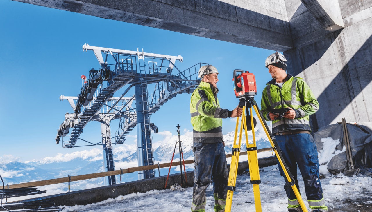 utsättningsverktyg mellan två byggare uppe bland snöiga berg och liftsystem