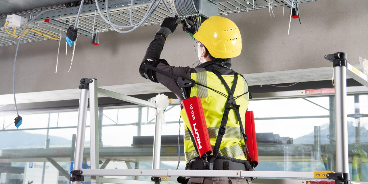 Elektriker installerar kablar ovanför huvudet utrustad med exoskelett för avlastning