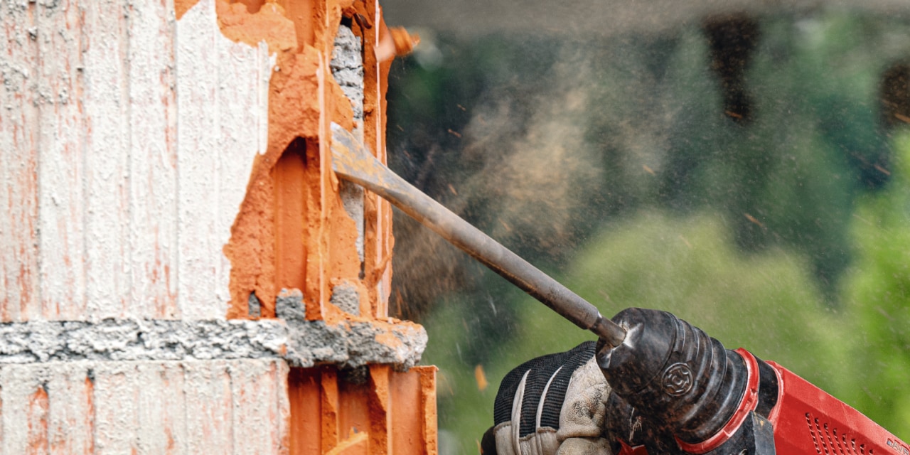 Red Hilti drill chipping into brick