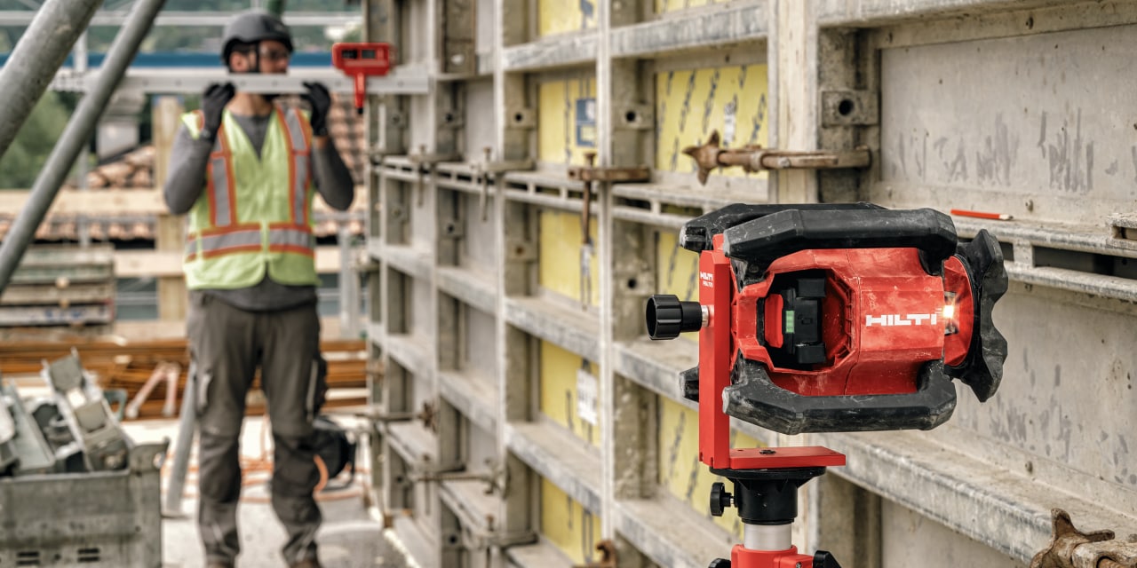 IMAGE SHOWS RED HILTI LASER LEVEL NEXT TO A WALL WITH PERSON IN THE BACKGROUND
