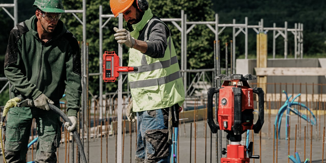 man holding a measuring rod next to a red hilti laser