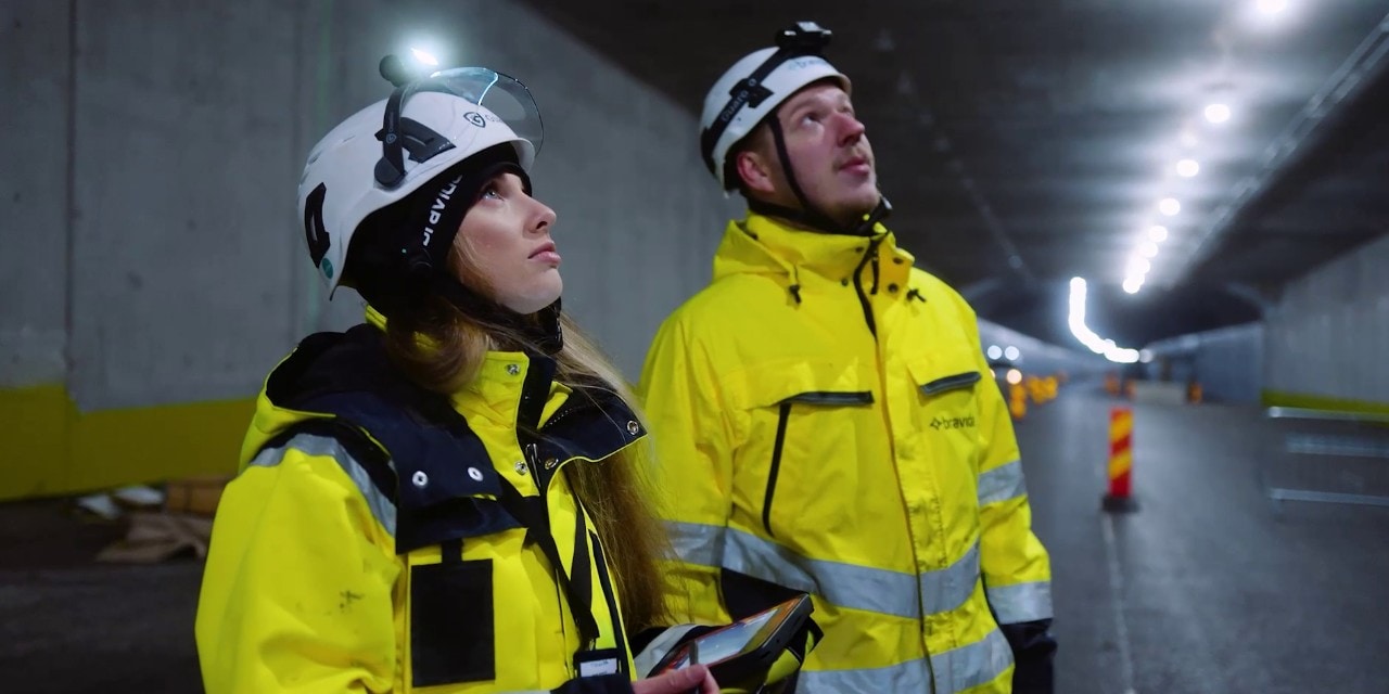 Två arbetare tittar upp mot taket i en vägtunnel