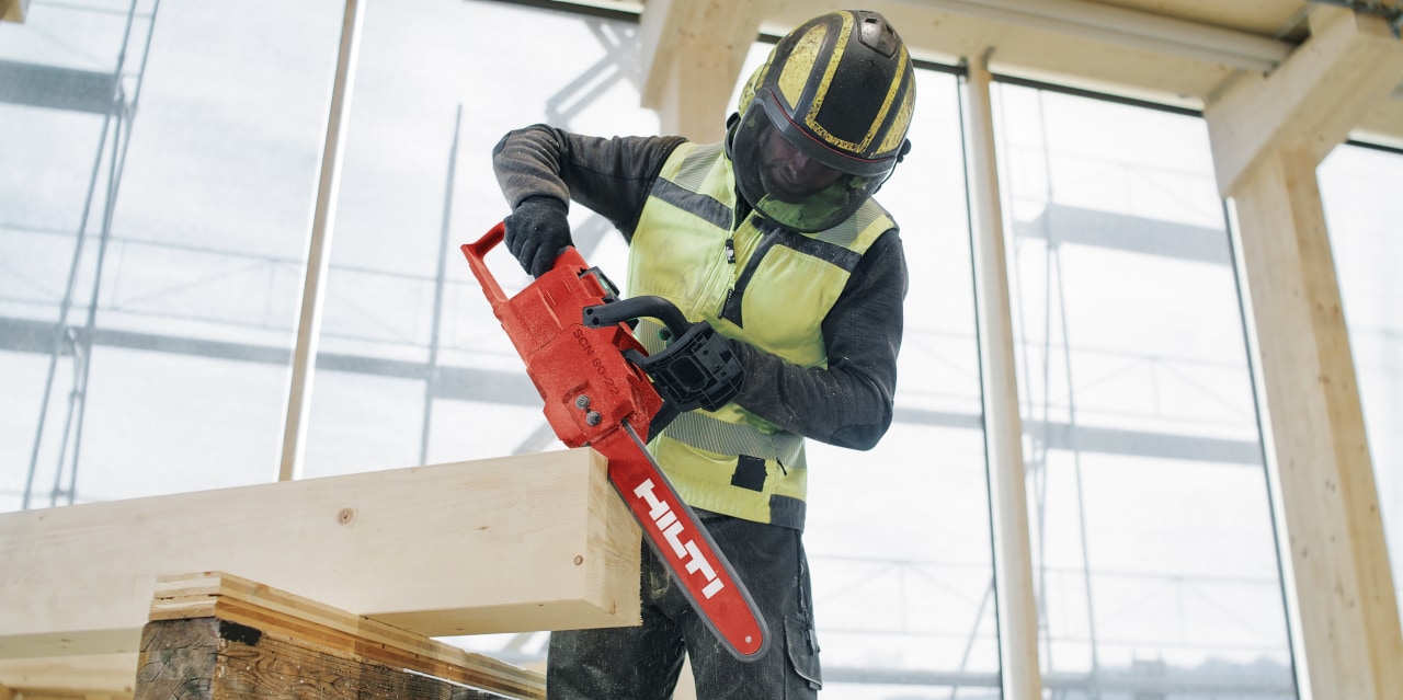 Arbetare i skyddsutrustning påbörjar sågning med motorsåg